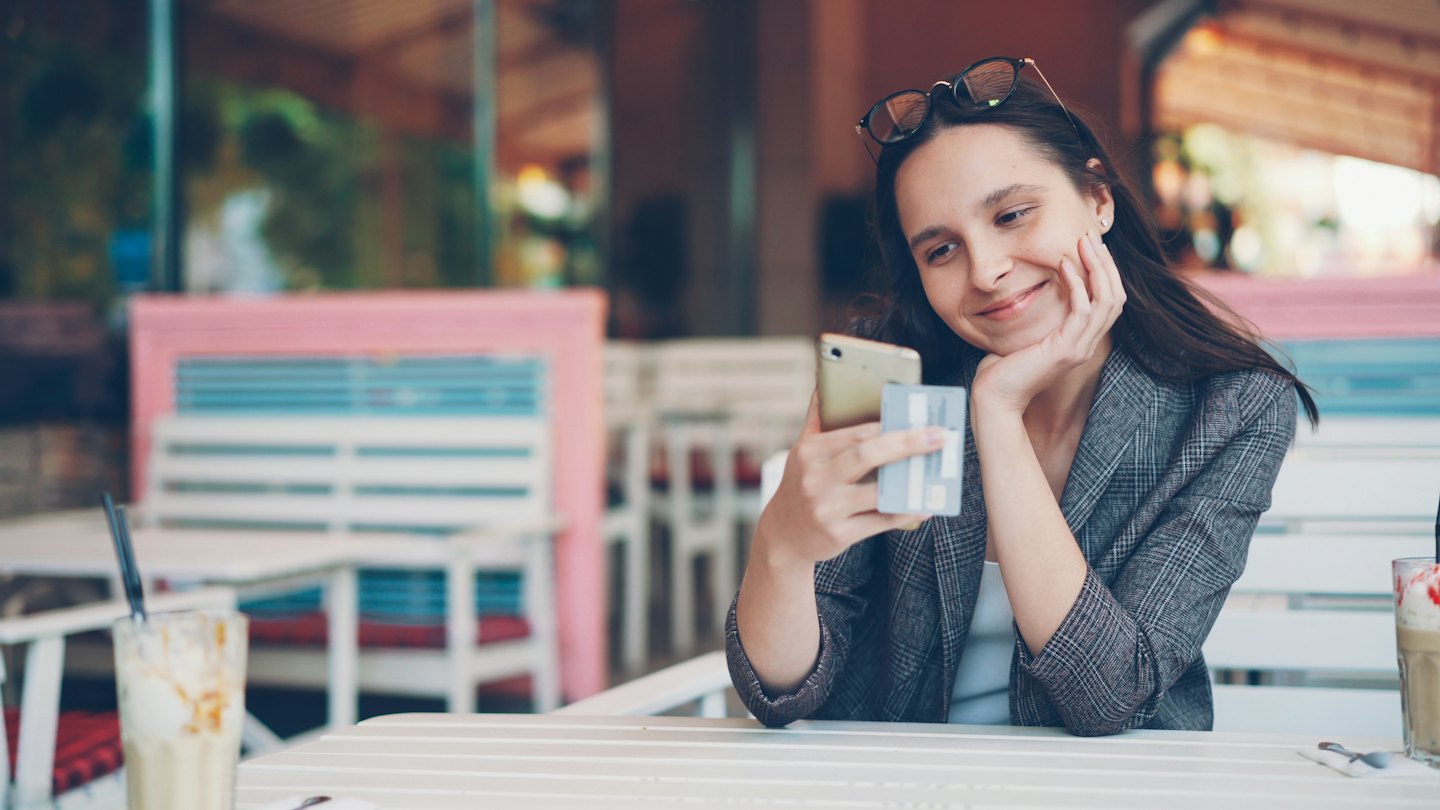 Woman holding a credit card while looking at her smartphone.