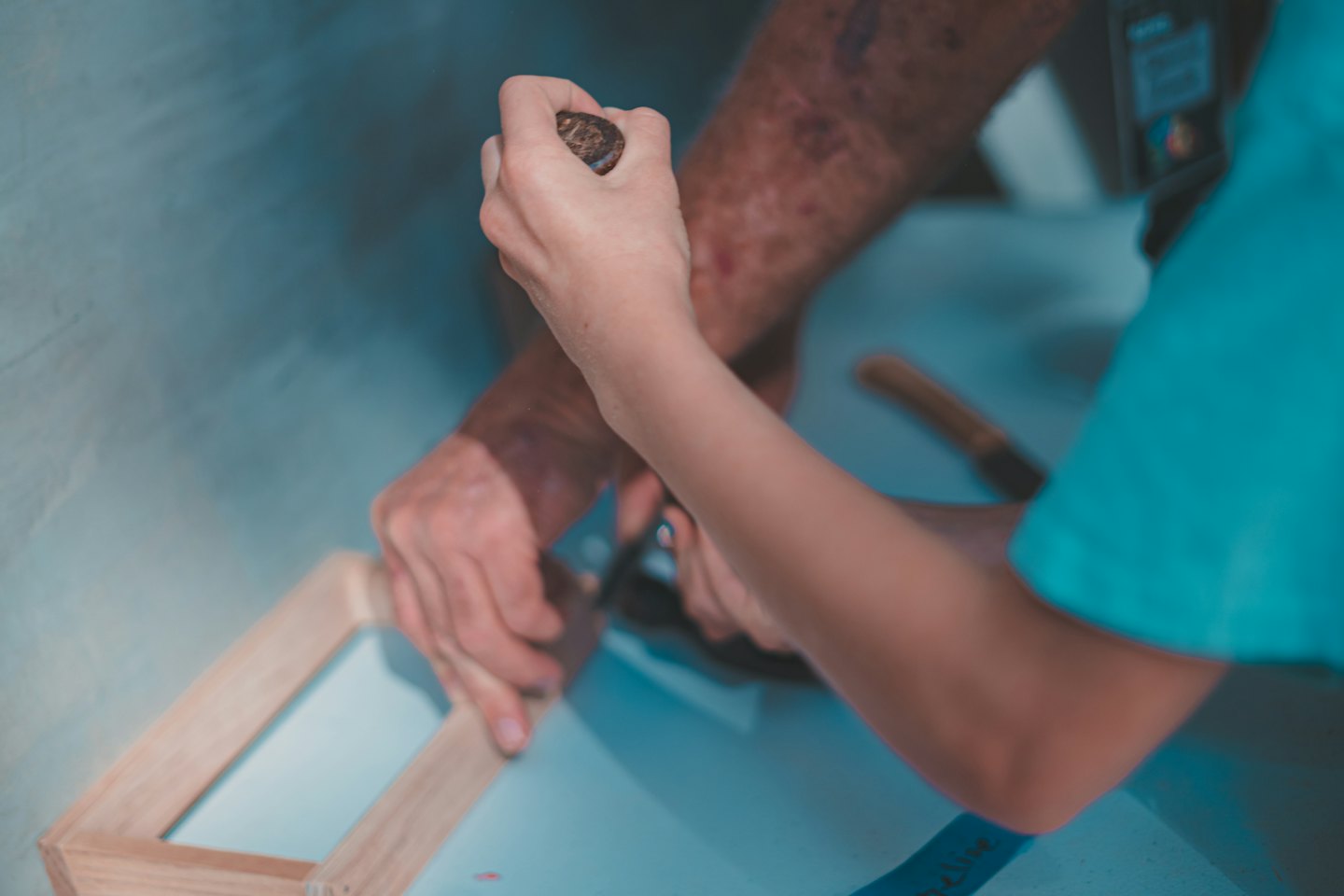 Two people's hands working together on a wooden craft project.